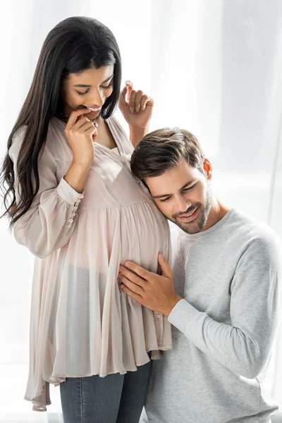 Bel homme étreignant et écouter ventre de sa femme africaine américaine enceinte — Photo de stock