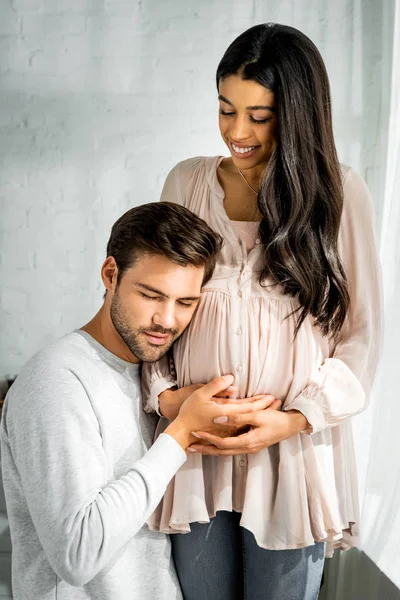 Bel homme étreignant et écouter ventre de sa femme africaine américaine enceinte — Photo de stock