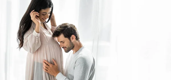 Foto panorámica de un hombre guapo abrazando el vientre de su mujer afroamericana embarazada - foto de stock