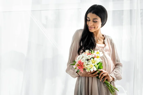 Smiling pregnant african american woman holding bouquet in apartment — Stock Photo
