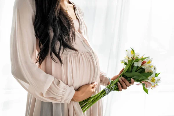 Vista recortada de mujer afroamericana embarazada sosteniendo ramo en apartamento - foto de stock