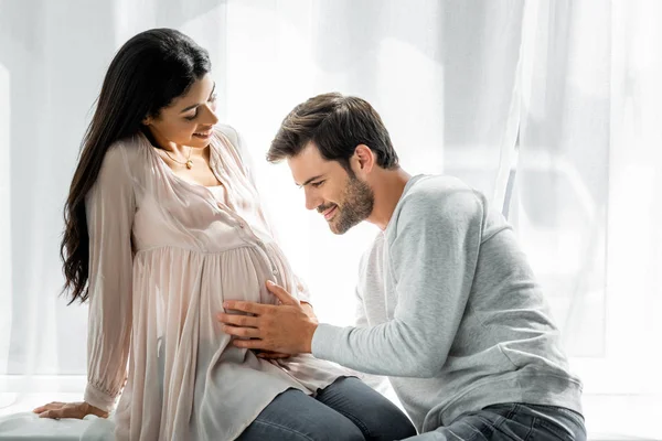 Guapo hombre abrazando vientre de su embarazada africana americana - foto de stock