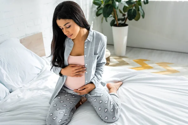 Femme afro-américaine enceinte en pyjama gris serrant le ventre — Photo de stock