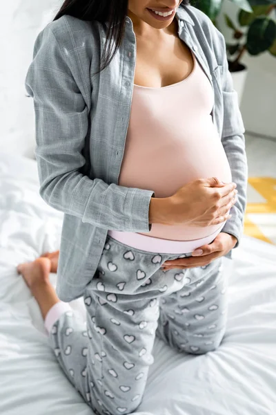 Vista recortada de mujer embarazada afroamericana en pijama abrazando el vientre - foto de stock