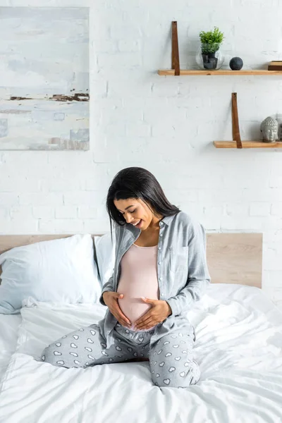 African american pregnant woman in pajamas smiling and hugging belly — Stock Photo