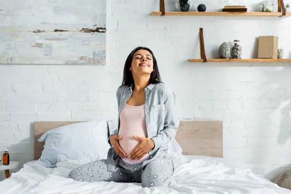 Mulher grávida afro-americana de pijama sorrindo e abraçando a barriga — Fotografia de Stock