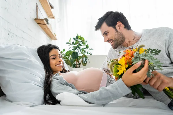 Handsome man holding bouquet and looking at his pregnant african american woman — Stock Photo