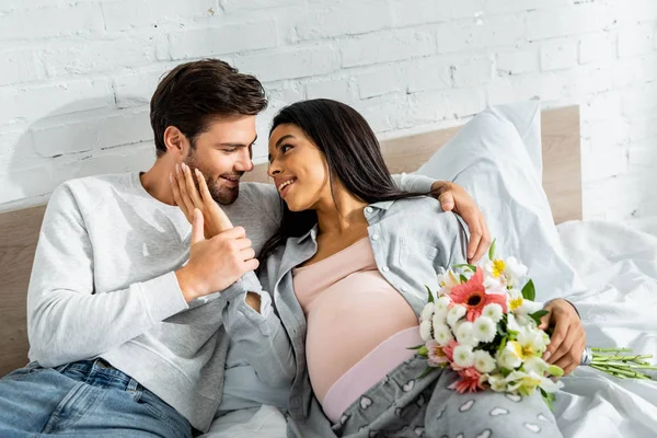 Bel homme étreignant sa femme enceinte afro-américaine avec bouquet — Photo de stock