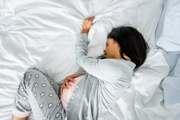 Top view of african american pregnant woman in pajamas touching belly and feeling pain — Stock Photo