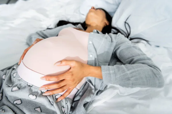 Selective focus of african american pregnant woman in pajamas touching belly and feeling pain — Stock Photo
