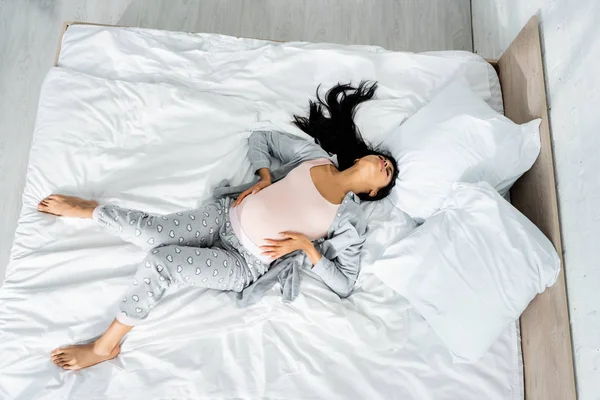 Top view of african american pregnant woman in pajamas touching belly and feeling pain — Stock Photo