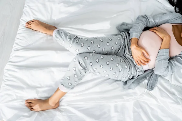Vista recortada de la mujer embarazada afroamericana en pijama tocando el vientre y sintiendo dolor - foto de stock