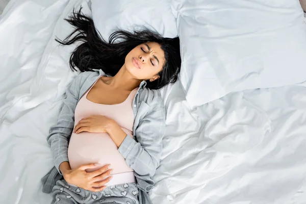 Vue du dessus de la femme enceinte afro-américaine en pyjama touchant le ventre et ressentant de la douleur — Photo de stock