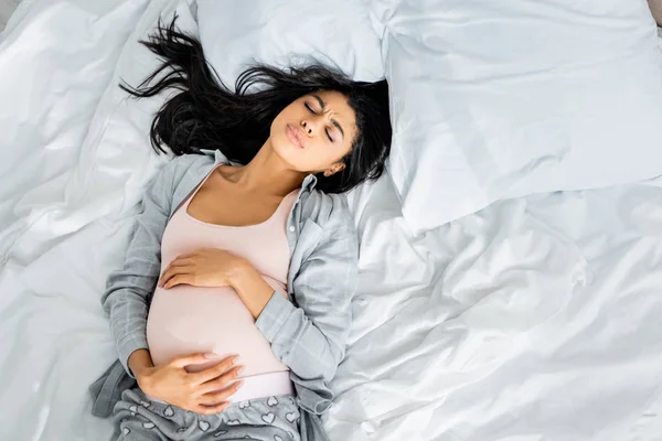 Top view of african american pregnant woman in pajamas touching belly and feeling pain — Stock Photo