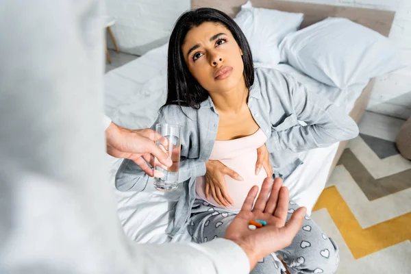 Abgeschnittene Ansicht eines Mannes, der schwangeren afrikanisch-amerikanischen Frau Pillen und ein Glas Wasser gibt — Stockfoto