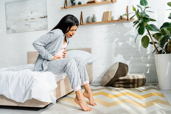 Mulher grávida afro-americana de pijama abraçando barriga e sentindo dor — Fotografia de Stock