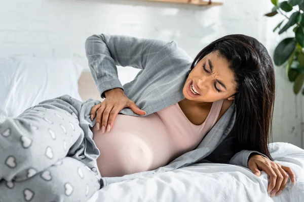 African american pregnant woman in pajamas touching belly and feeling pain — Stock Photo