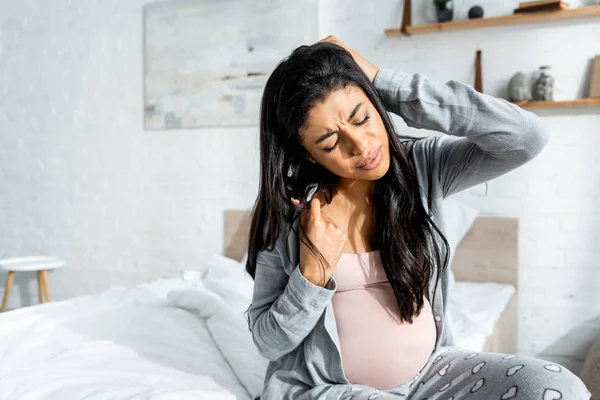 Mujer embarazada afroamericana en pijama sintiendo dolor en apartamento - foto de stock