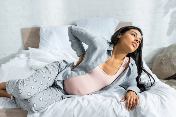 African american pregnant woman in pajamas feeling pain and lying on bed — Stock Photo