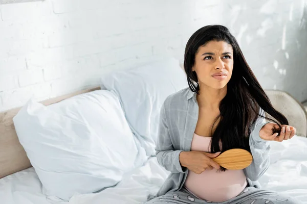 Arrabbiato americano donna incinta in pigiama tenendo spazzola per capelli in appartamento — Foto stock