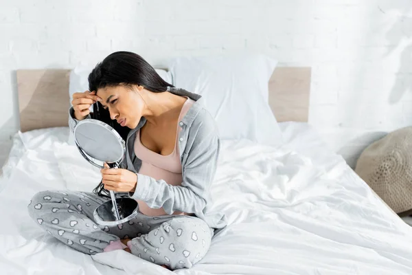 African american pregnant woman in pajamas looking at mirror and touching face in apartment — Stock Photo