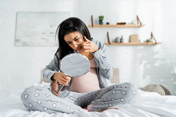 Afroamericano donna incinta in pigiama guardando specchio e toccando il viso in appartamento — Foto stock