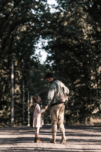 Мужчина, держащий за руки ребенка, стоя на дороге, постафокалиптическая концепция — стоковое фото