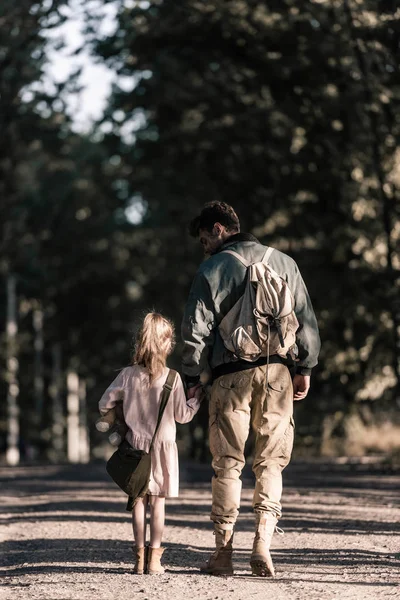 Вид сзади ребенка, держащегося за руки с мужчиной, стоя на дороге, пост-апокалиптическая концепция — стоковое фото