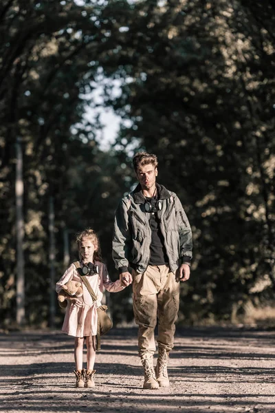 Niedliches Kind hält Händchen mit Mann, während es Teddybär hält, postapokalyptisches Konzept — Stockfoto