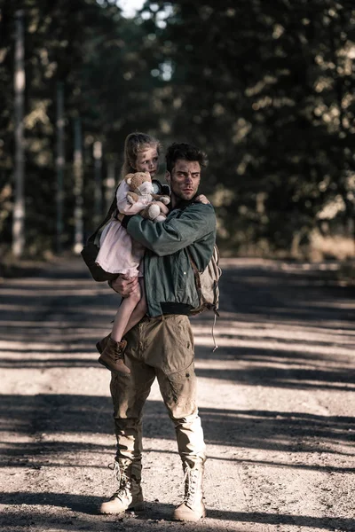 Hombre guapo y sucio sosteniendo en brazos niño en chernobyl, concepto post apocalíptico - foto de stock