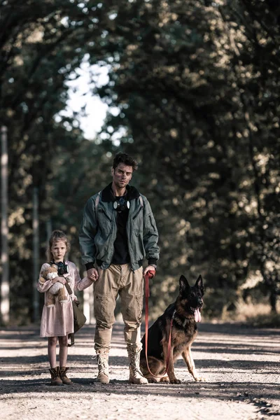 Schöner Mann hält Händchen mit Kind in der Nähe von Schäferhund, postapokalyptisches Konzept — Stockfoto