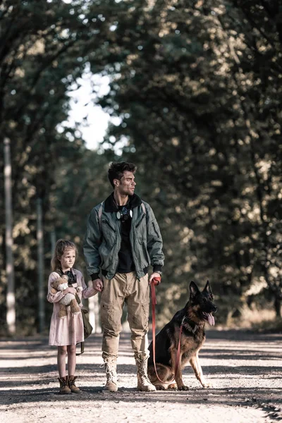 Hombre cogido de la mano con el niño cerca de perro pastor alemán, concepto post apocalíptico - foto de stock