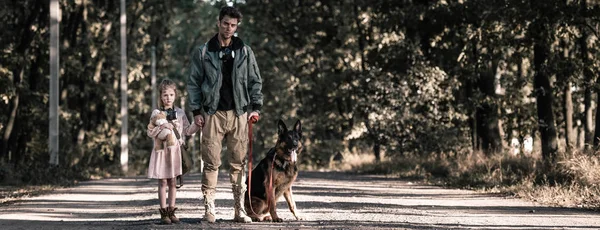 Colpo panoramico di uomo che si tiene per mano con bambino vicino cane pastore tedesco, concetto post apocalittico — Foto stock