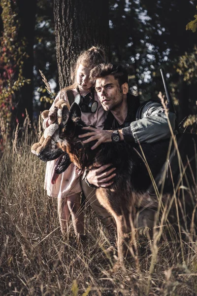 Selektiver Fokus eines schmutzigen Mannes, der einen Schäferhund in der Nähe eines Kindes berührt, postapokalyptisches Konzept — Stockfoto