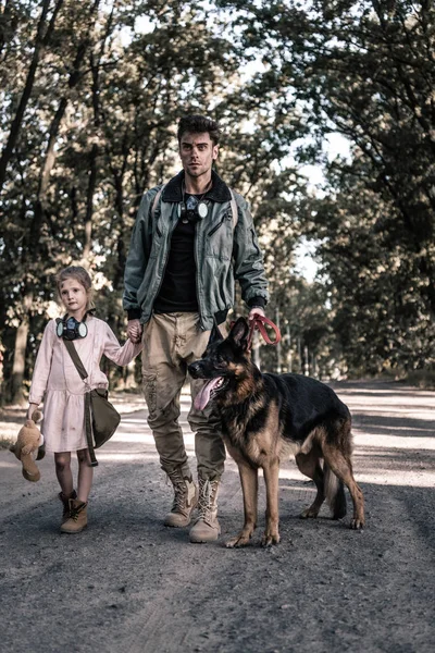 Hombre cogido de la mano con el niño y caminar con el perro pastor alemán, concepto post apocalíptico - foto de stock