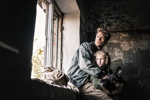 Man hugging dirty kid near german shepherd dog in abandoned building, post apocalyptic concept — Stock Photo