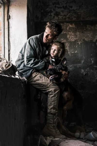Man hugging dirty child near german shepherd dog in abandoned building, post apocalyptic concept — Stock Photo