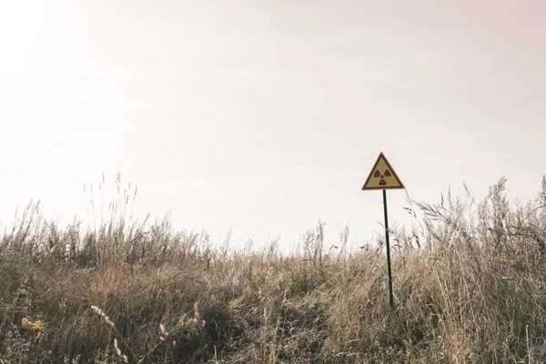 Triángulo con símbolo tóxico de advertencia cerca del campo, concepto post apocalíptico - foto de stock