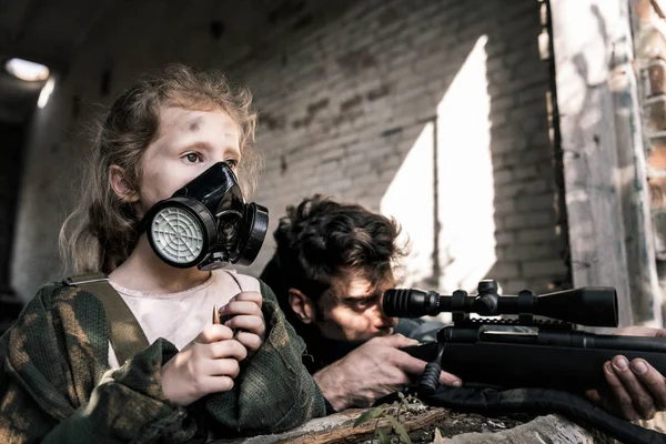 Selective focus of kid in gas mask near man with gun, post apocalyptic concept — Stock Photo