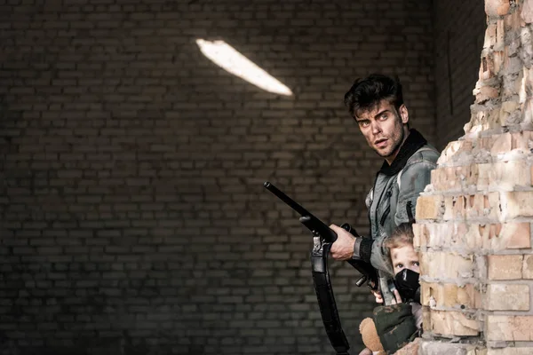 Bel homme tenant pistolet près du bâtiment abandonné, concept post apocalyptique — Photo de stock