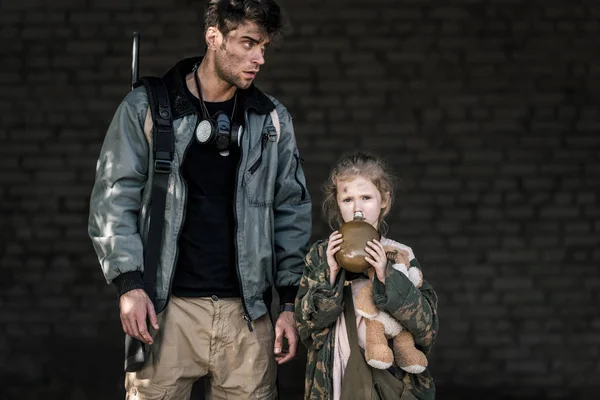 Hombre guapo de pie cerca de niño con frasco, concepto post apocalíptico - foto de stock