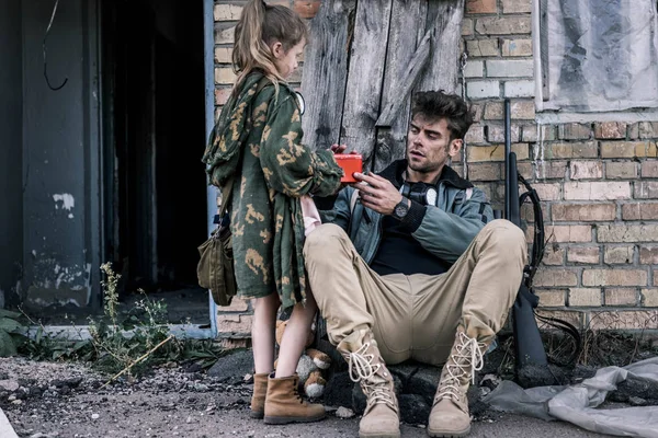 Niño de pie cerca de hombre armado con botiquín de primeros auxilios, concepto post apocalíptico - foto de stock