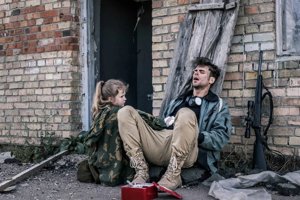 Kid holding medical bandage near man sitting on ground, post apocalyptic concept — Stock Photo