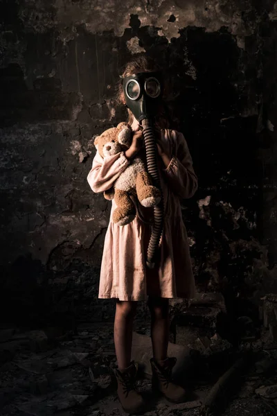 Kid in gas mask standing and holding teddy bear, post apocalyptic concept — Stock Photo