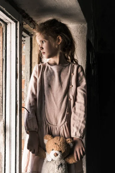 Bambino frustrato tenendo orsacchiotto vicino alla finestra, concetto post apocalittico — Foto stock
