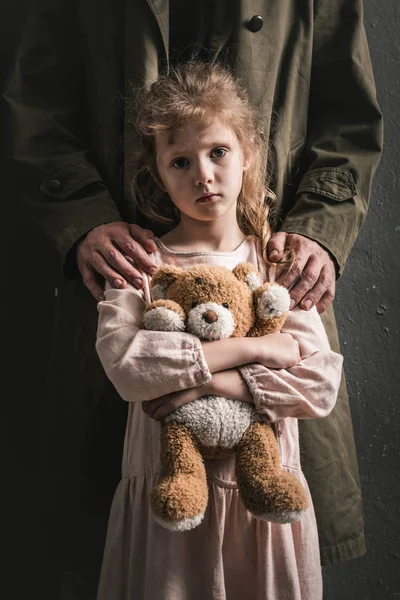 Vista recortada del hombre de pie cerca de niño con osito de peluche, concepto post apocalíptico - foto de stock