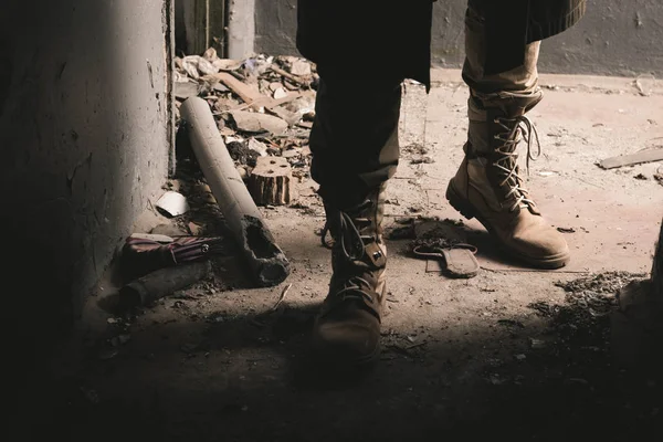 Vista recortada del hombre en botas de pie en la habitación erosionada, concepto post apocalíptico - foto de stock