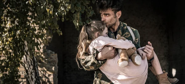 Panoramic shot of man holding in arms and kissing kid with teddy bear, post apocalyptic concept — Stock Photo