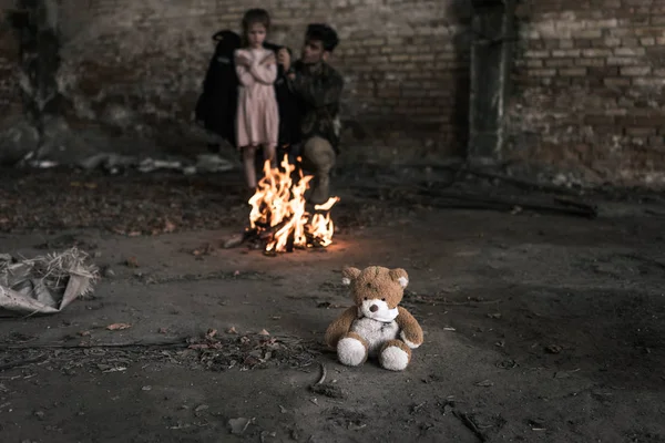 Selective focus of teddy bear near man and child in building, post apocalyptic concept — Stock Photo