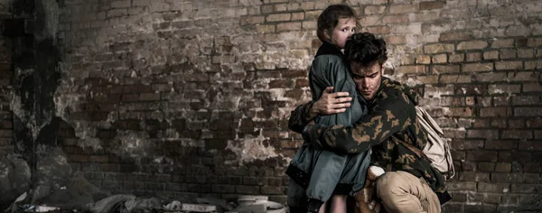 Panoramic shot of handsome man hugging child near brick wall, post apocalyptic concept — Stock Photo